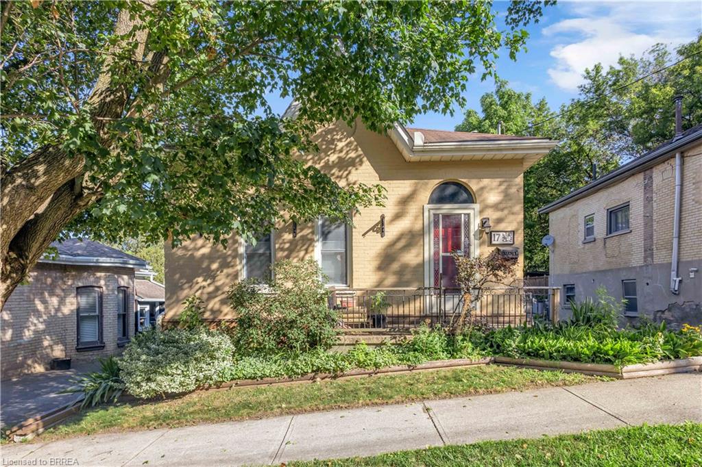 Light-toned brick exterior with an arched entry door and a covered front porch featuring wrought iron railing