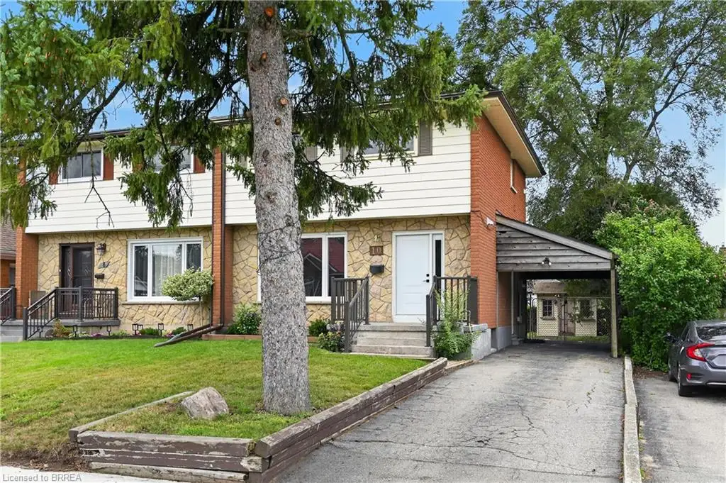 Brick and stone facade, covered carport, mature trees, concrete driveway, and front lawn