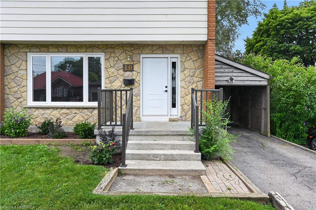 Stone veneer facade with siding accents, concrete steps with metal railings, white front door with sidelight, and an attached carport