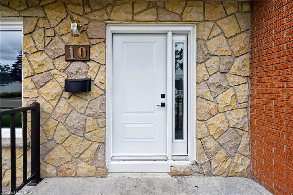 Stone and brick exterior featuring a white paneled front door with a sidelight, a bronze exterior light fixture, and a black mailbox