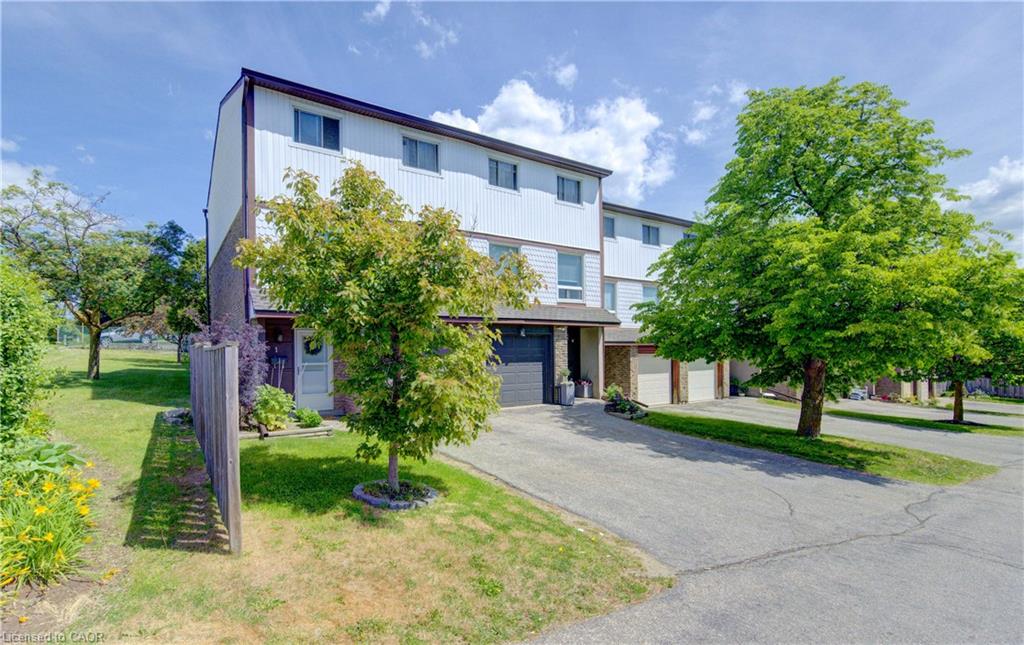 Townhome exterior featuring a detached garage, private driveway, side yard, and mature trees