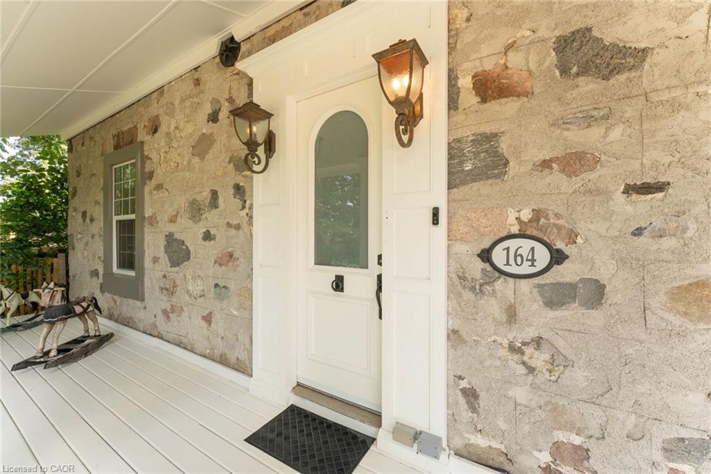 Stone-clad exterior featuring a white paneled front door with an arched glass insert, two wall-mounted lanterns, and a white porch with a paneled ceiling