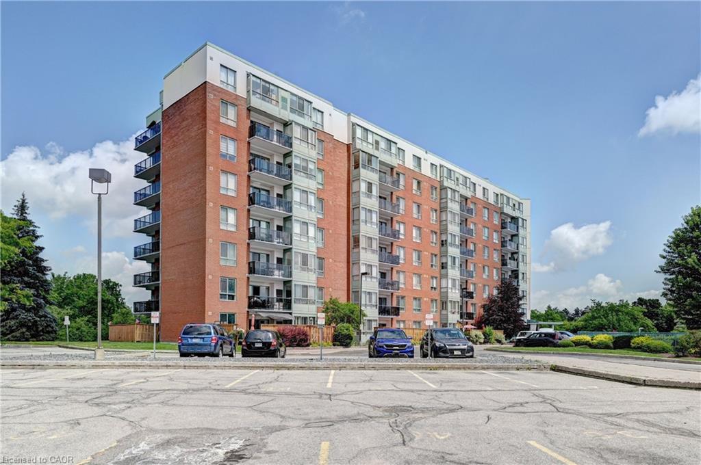 Multi-story building featuring brick and light-toned siding, individual balconies with glass railings, and a surface parking lot