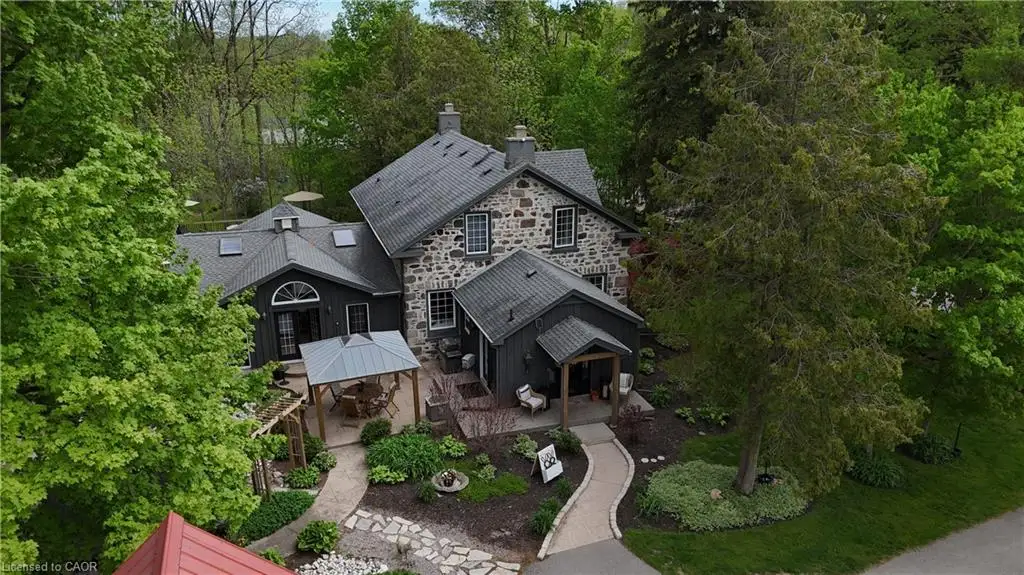 Stone facade home featuring multiple gabled roofs, natural stone pathways, mature trees, and a covered patio area