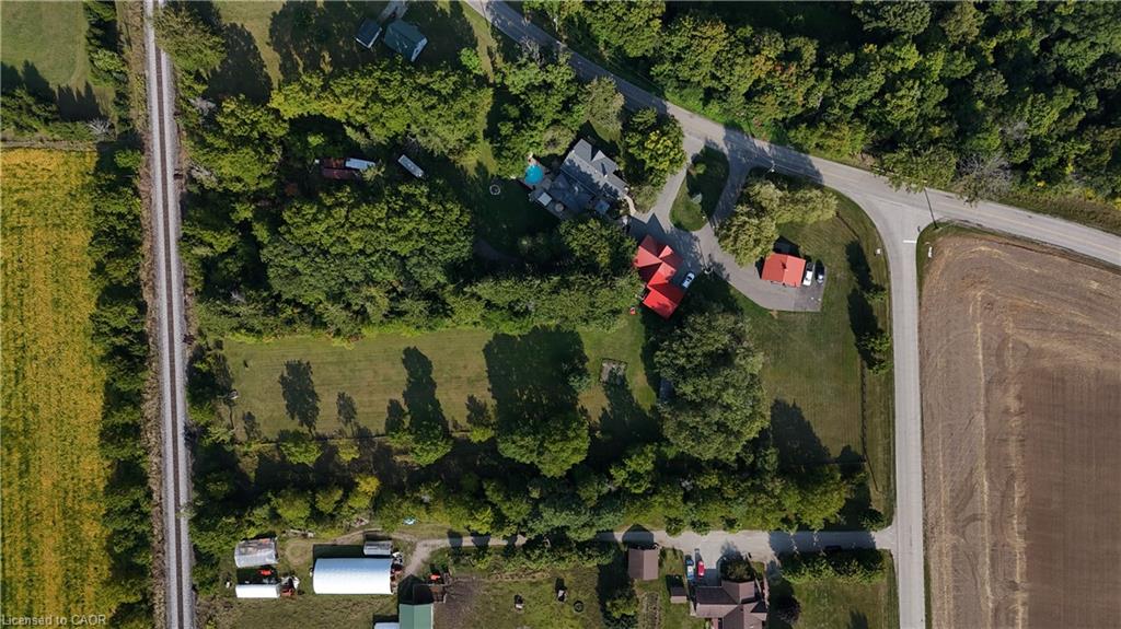 Expansive aerial showcasing a significant land parcel with two distinct structures, mature trees, and a paved road frontage