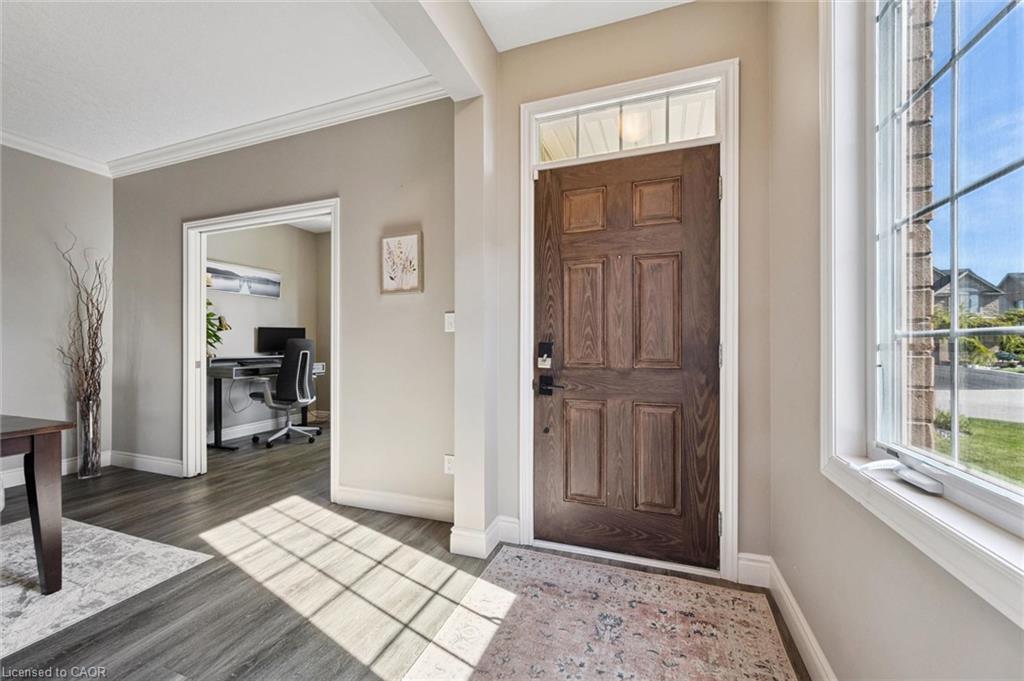 Wood-finish flooring, paneled front door with transom window, window with divided lites, crown molding, and a cased opening