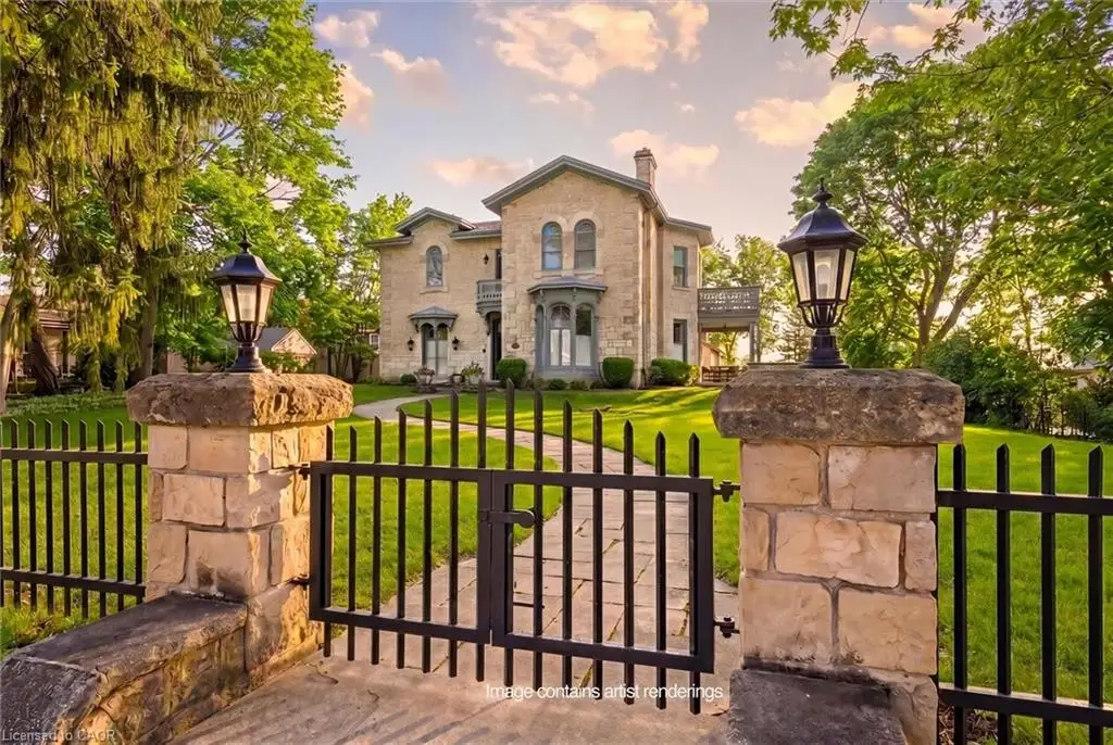 Stone masonry home with a wrought iron fence and gate, featuring two-story bay windows, a covered porch, and a second-story balcony