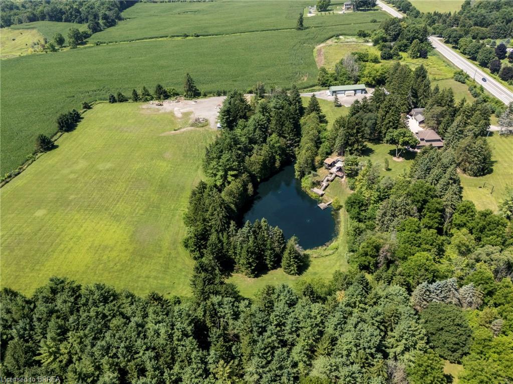 Expansive natural property featuring a private pond, surrounding mature trees, a manicured lawn, and a gravel area