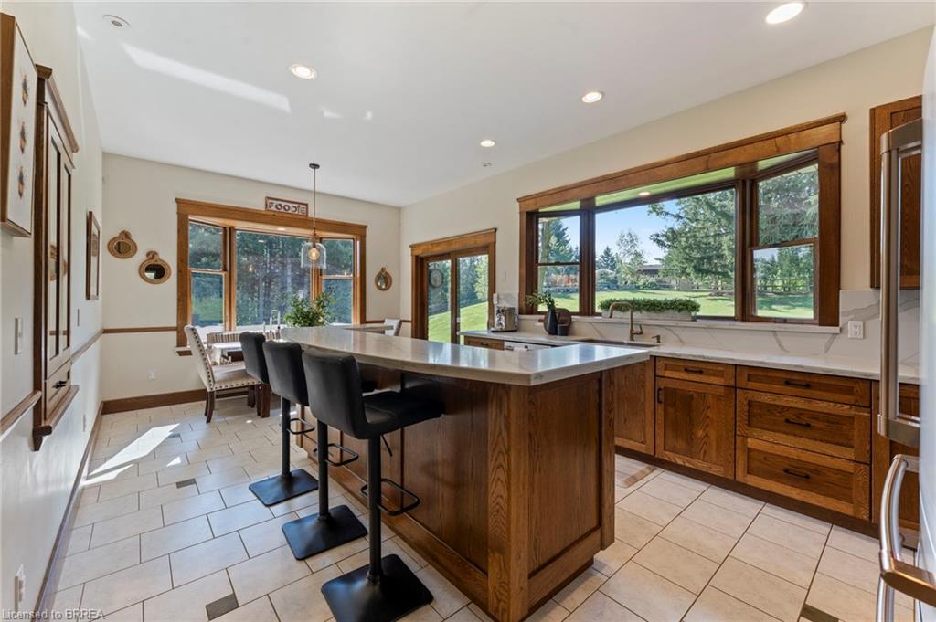 Spacious kitchen featuring a large central island with seating, extensive wood cabinetry, white countertops with matching backsplash, and tile flooring with dark accent squares
