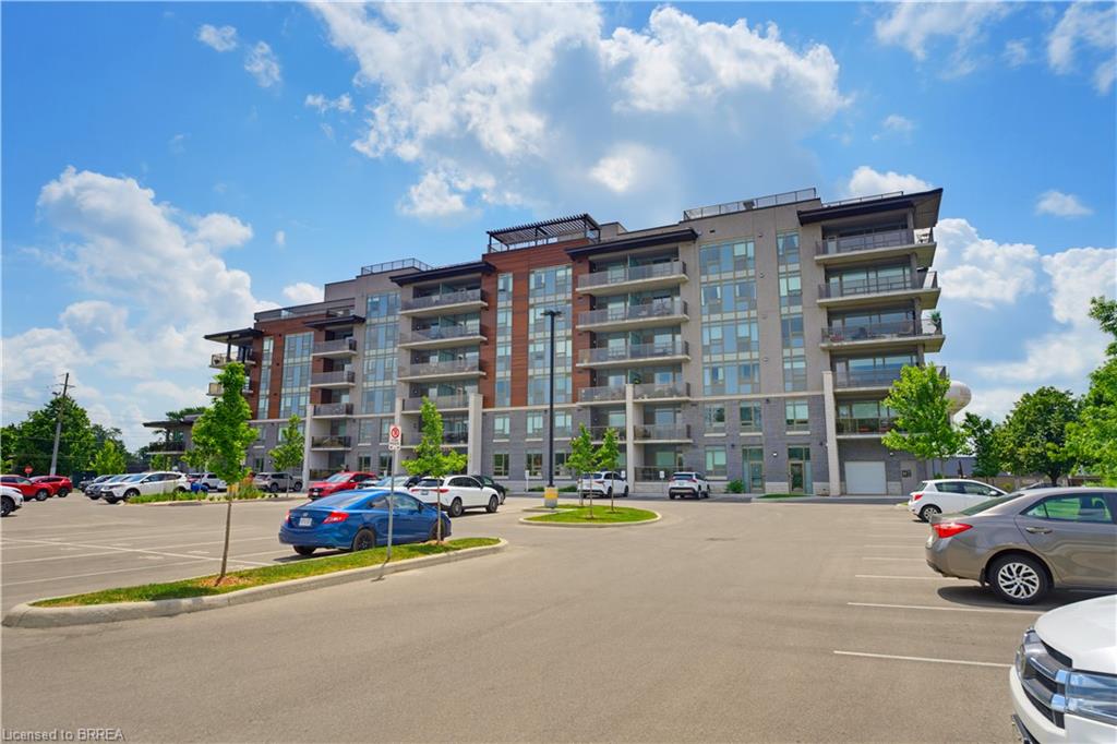 Contemporary multi-story building featuring brick and stone cladding, multiple private balconies with glass railings, and a surface parking lot
