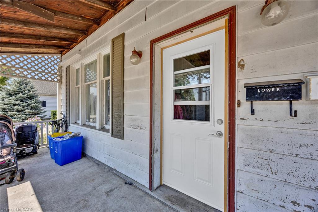 Covered front porch featuring white horizontal siding with wood-trim framing, multiple multi-pane windows with wood casings, a white entry door with wood surround, and a "TOWER" wall-mounted sign