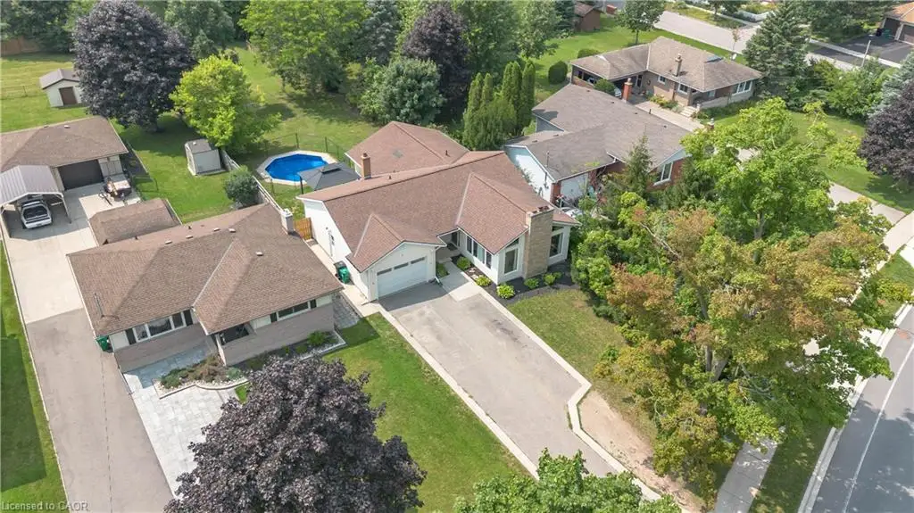 Aerial perspective featuring a multi-building residential lot with asphalt driveways, a detached garage, a covered carport, and an above-ground swimming pool situated on a landscaped parcel with mature trees