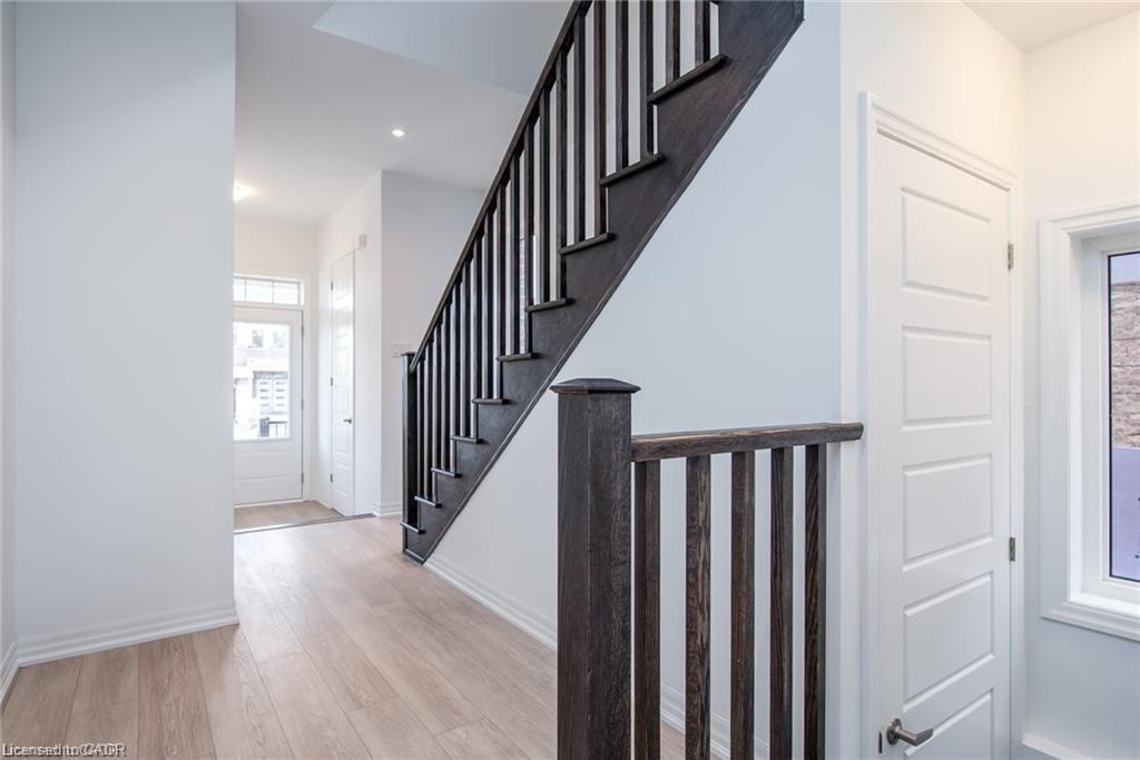 Entryway featuring light wood-finish flooring, a dark wood staircase with matching railing, recessed lighting, a paneled entry door with glass insert, and a white paneled interior door