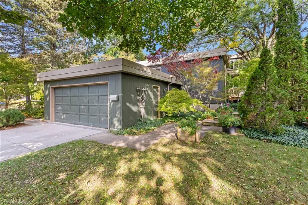 Exterior featuring a detached garage with paneled door, concrete driveway, and mature landscaping