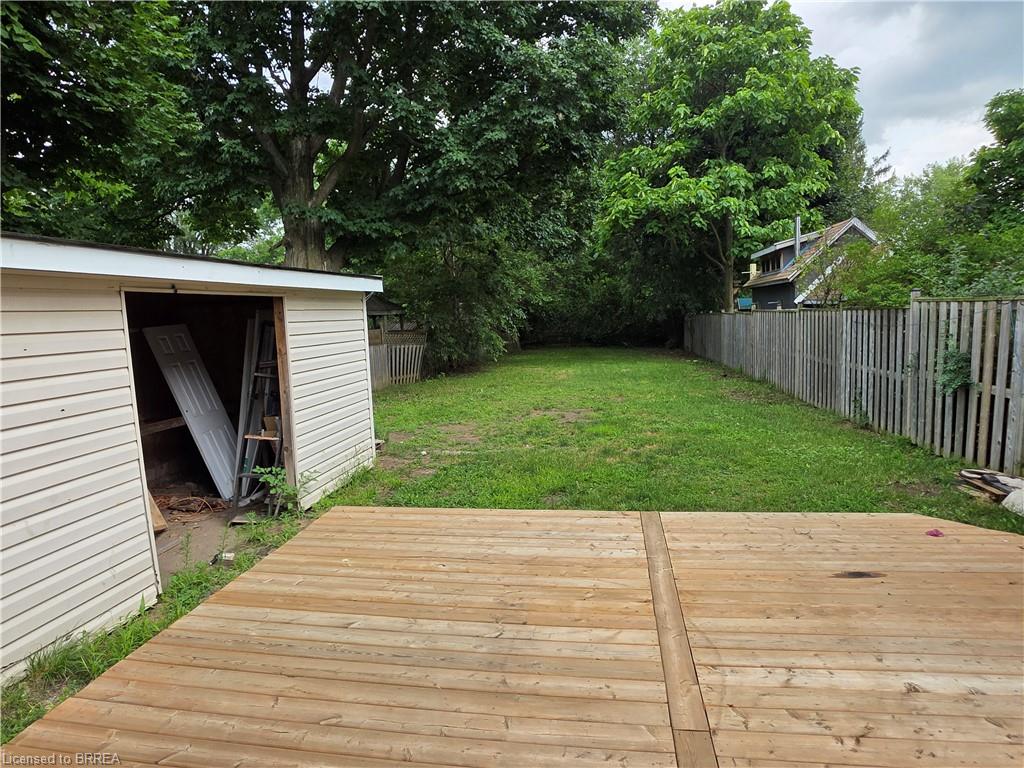 Spacious backyard featuring a wood deck, expansive lawn, storage shed with vinyl siding, wood privacy fencing, and mature trees providing natural screening