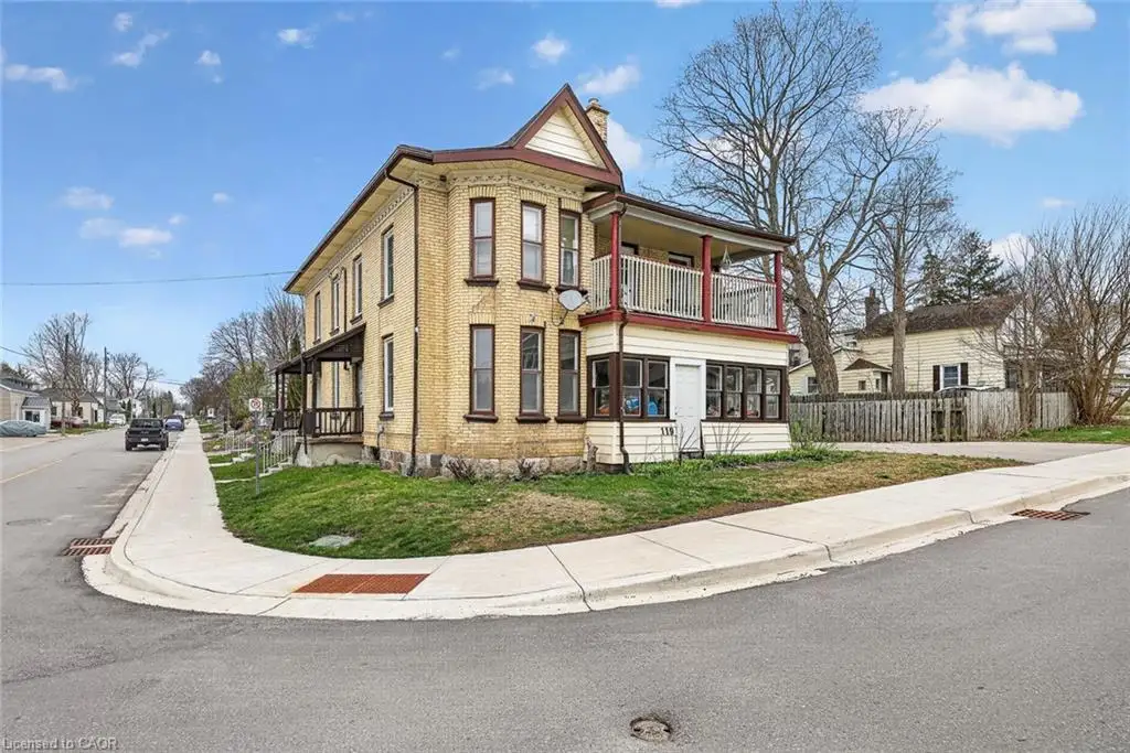 Traditional architecture featuring a brick exterior, a covered porch, a second-story balcony with white railing, a sunroom, and multiple windows