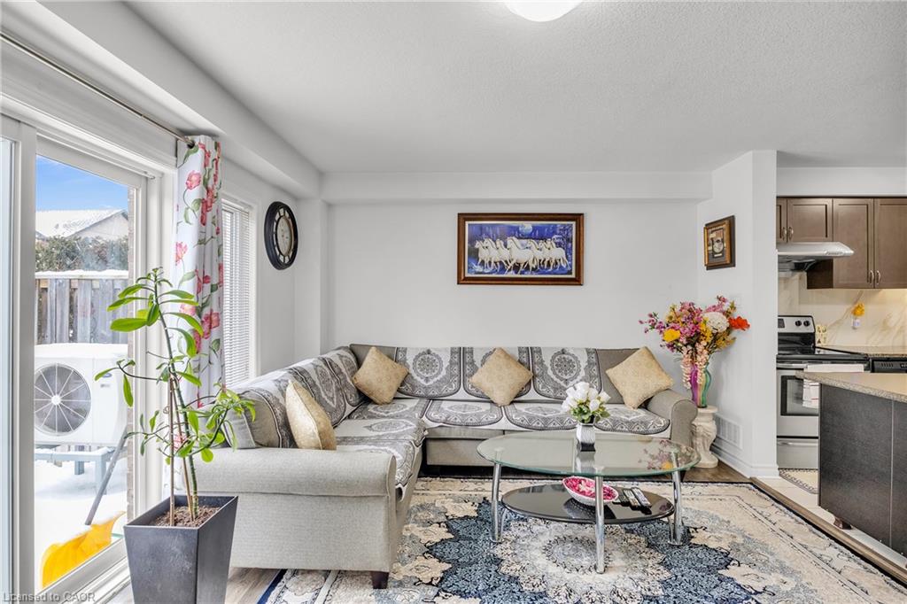 Bright open-concept living area featuring a neutral color palette, built-in kitchen with stainless steel appliances, large sliding glass doors with mountain backdrop access, geometric area rug, and abundant natural light from expansive windows
