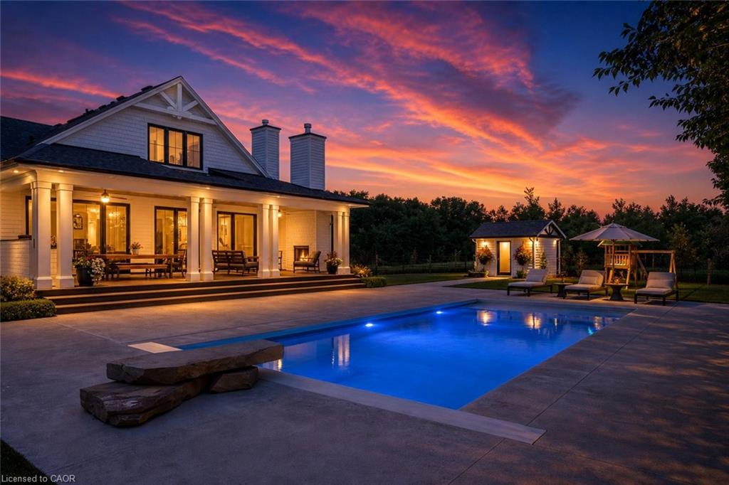 Rear exterior featuring a large rectangular swimming pool with a stone diving platform, expansive concrete patio, and a covered porch with architectural columns