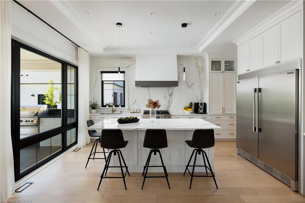 Gourmet kitchen featuring a large central island, white cabinetry, integrated stainless steel appliances, a range hood with a marble-finish backsplash, and light wood-finish flooring