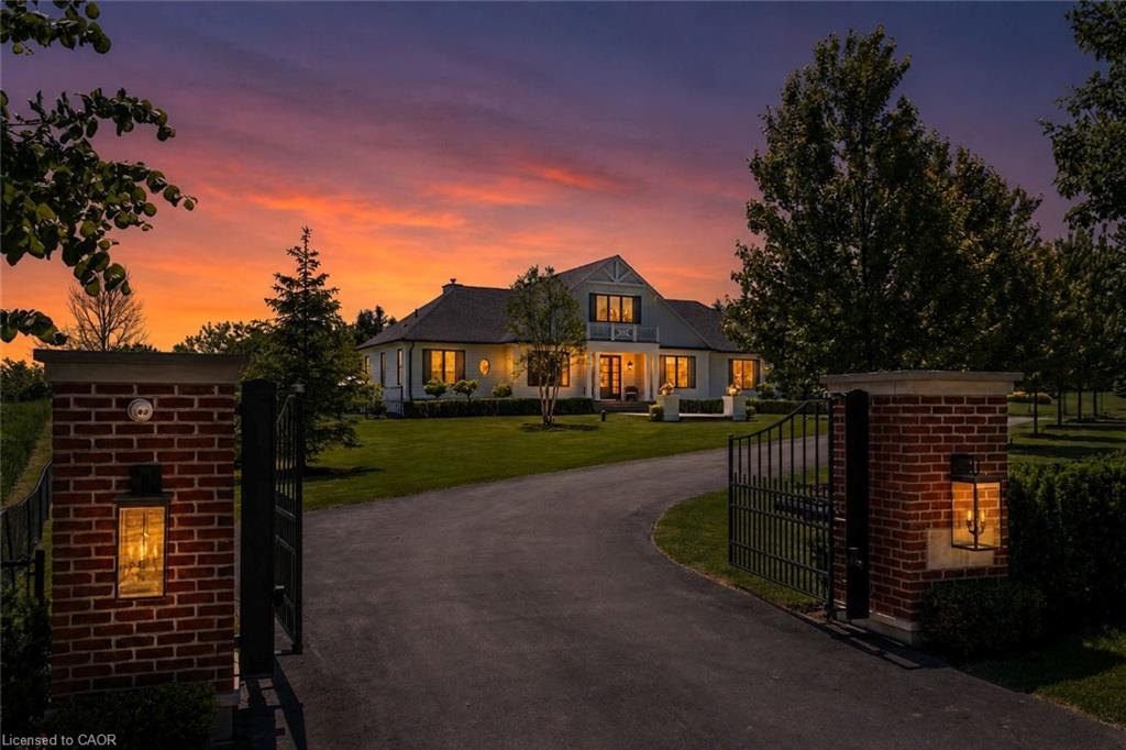 Gated entry with brick columns and integrated lanterns, asphalt driveway, expansive lawn, and mature trees
