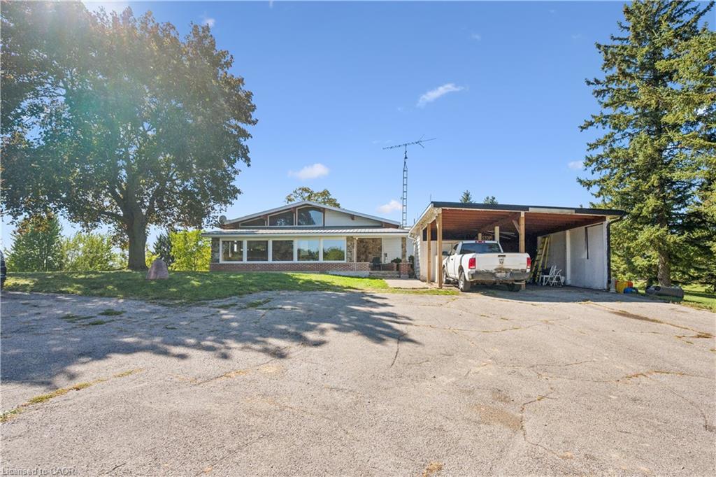 Expansive asphalt driveway, attached carport, and a prominent front-facing house with multiple windows