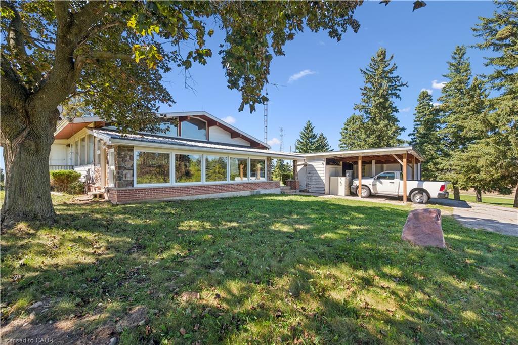 Property with expansive windows, stone and brick exterior accents, a detached carport, and mature trees