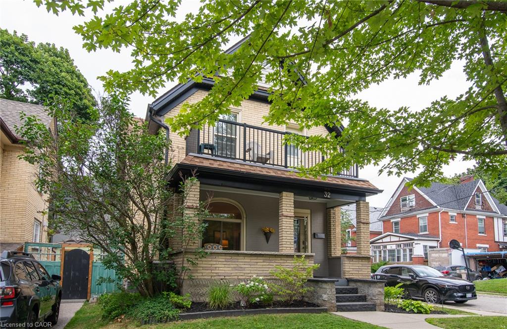 Brick-clad exterior featuring a covered front porch with brick pillars, a second-story balcony with dark railings, and a prominent front door with side windows
