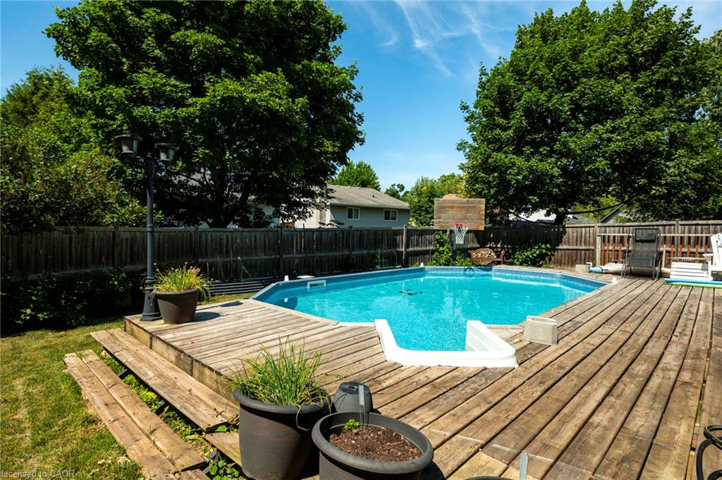Expansive backyard featuring a large above-ground pool, surrounding wood-finish decking, and mature trees