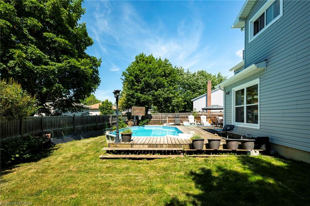 Expansive backyard featuring a manicured lawn, a swimming pool with a surrounding wood deck, and a privacy fence