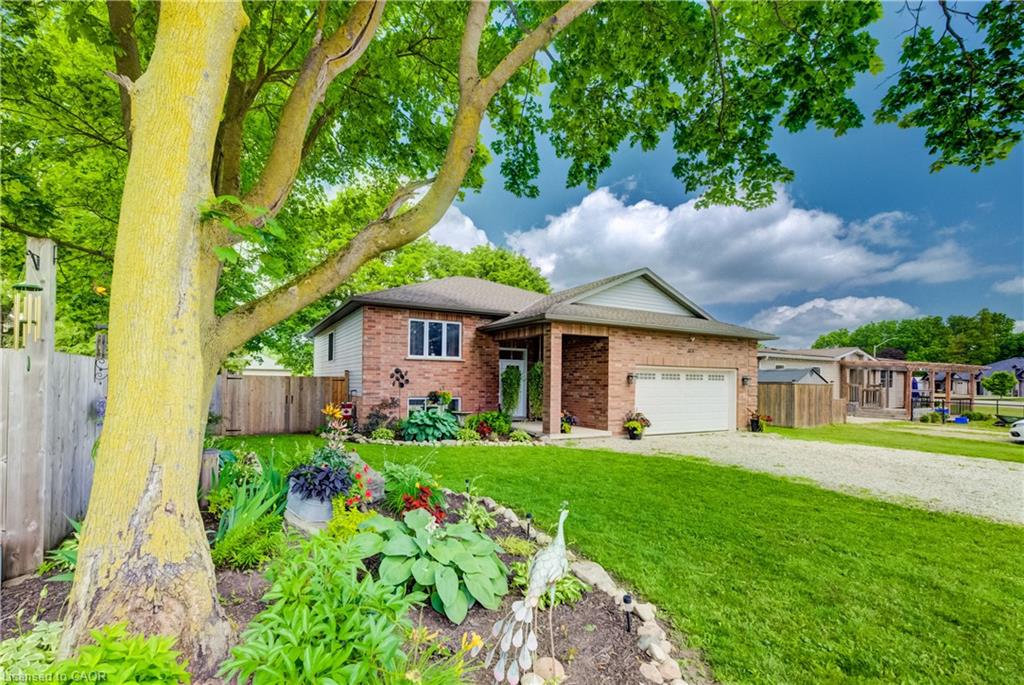 Brick exterior home featuring an attached garage, landscaped front yard with established plantings, and a gravel driveway