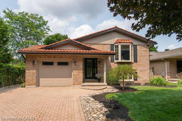 Brick exterior with a terracotta-style roof, an integrated garage, a bay window with shutters, and a paver driveway
