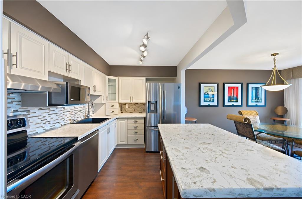 Open-concept kitchen featuring an island with a light-toned countertop, wood-finish flooring, white cabinetry, stainless steel appliances, and a tiled backsplash