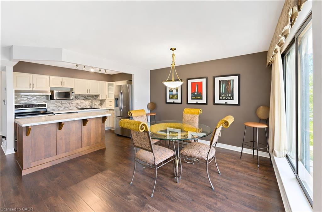 Open-concept living space featuring wood-finish flooring, a kitchen island with a stone-look countertop, stainless steel appliances, and a tiled backsplash