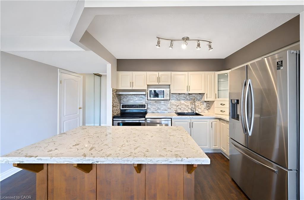 Kitchen featuring a large central island with a light-toned countertop, a stainless steel French door refrigerator, white cabinetry, a tiled backsplash, and wood-finish flooring