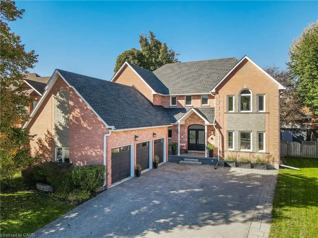 Multi-level brick exterior featuring a three-car garage, stone masonry accents, a covered front entryway, and a paved stone driveway
