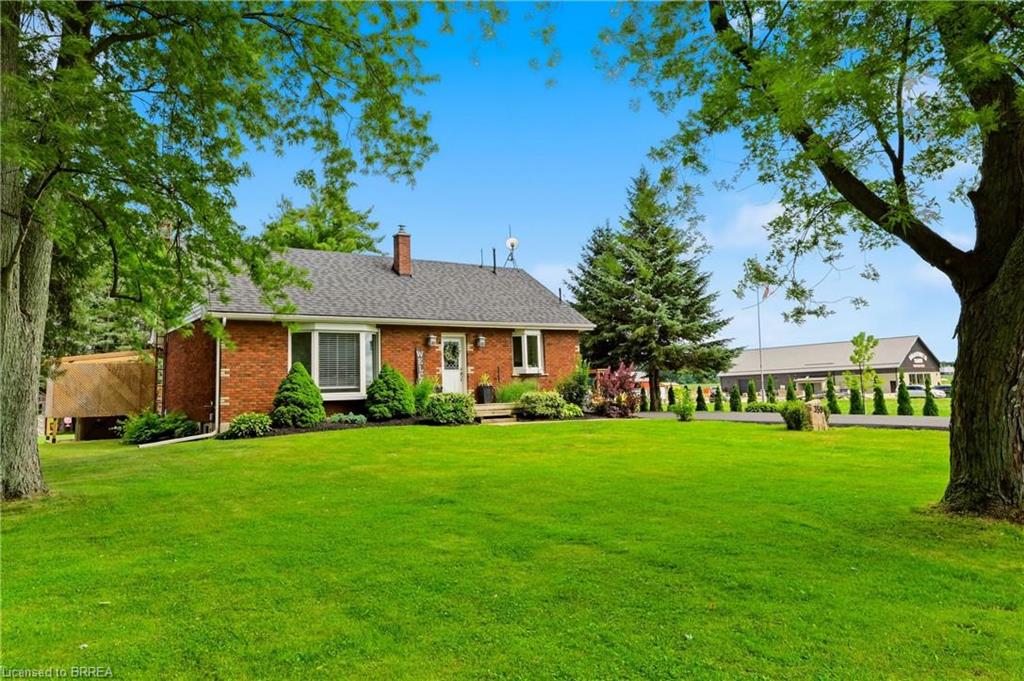 Brick exterior with a shingled roof, bay window, landscaped foundation plantings, and an expansive lawn