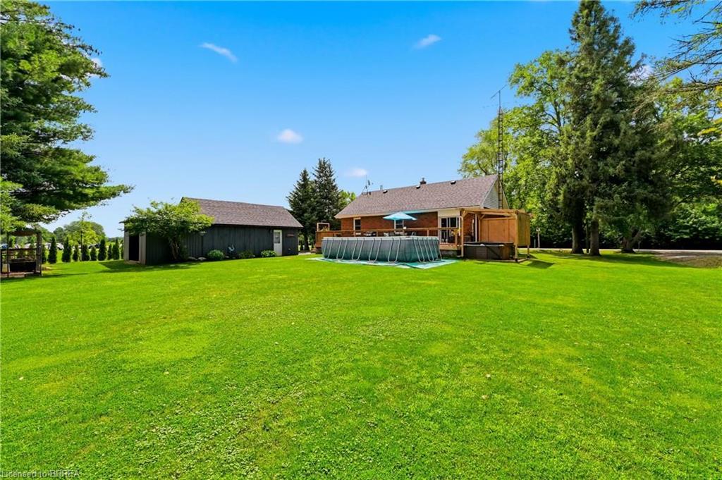 Expansive green lawn with mature trees, a detached storage building, and a rear deck with an above-ground pool