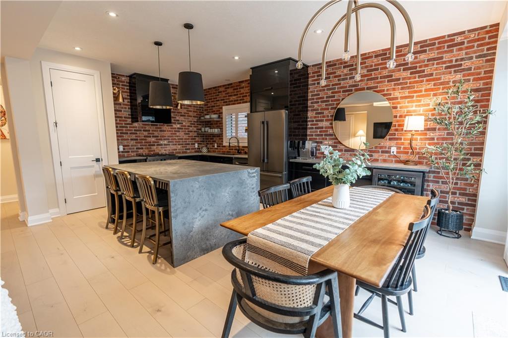 Exposed brick accent wall, light wood-finish flooring, large kitchen island with seating, stainless steel appliances, and built-in wine cooler
