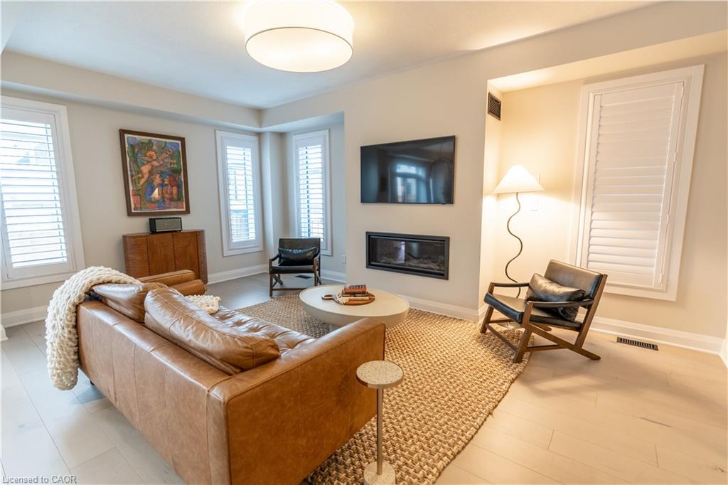 Recessed electric fireplace, light wood-finish flooring, bay window, plantation shutters, and a ceiling-mounted light fixture