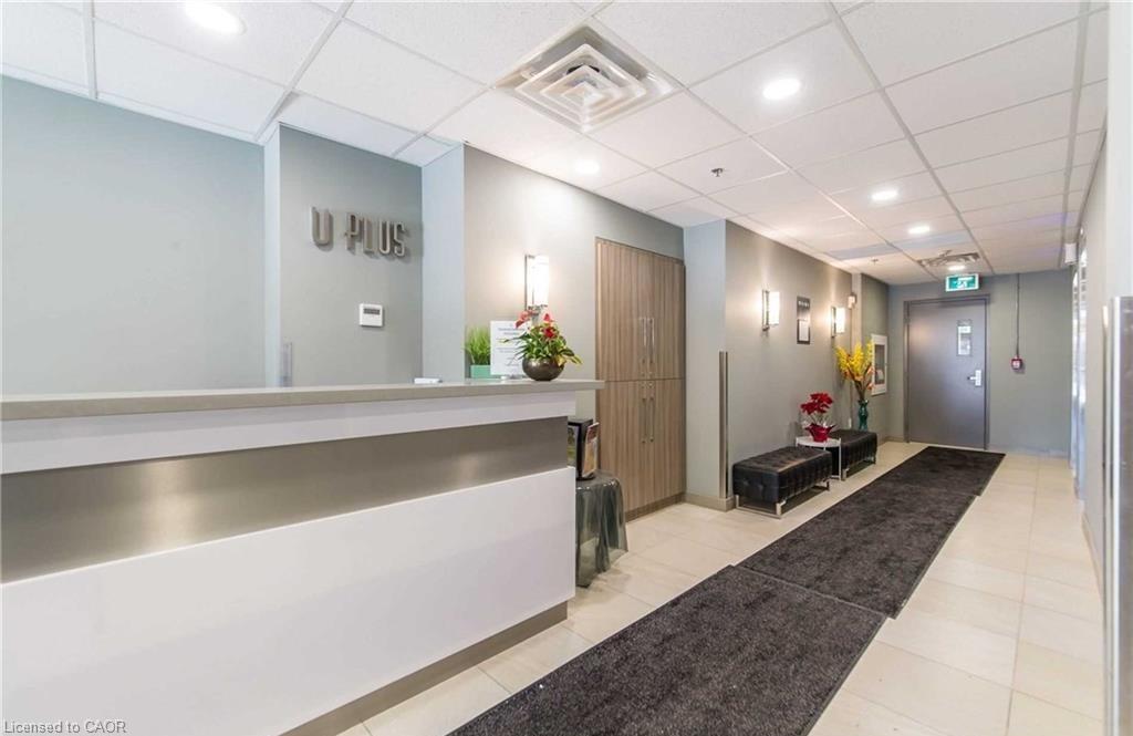 Modern reception area featuring a white and silver-toned desk, recessed ceiling lighting, textured wall sconces, wood-look cabinetry, and light-toned tile flooring