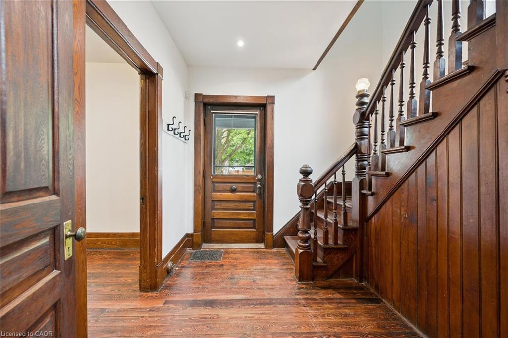 Foyer featuring wood-finish flooring, a traditional wood staircase with balusters, wood paneling, a wood entry door with glass upper portion, and wood trim