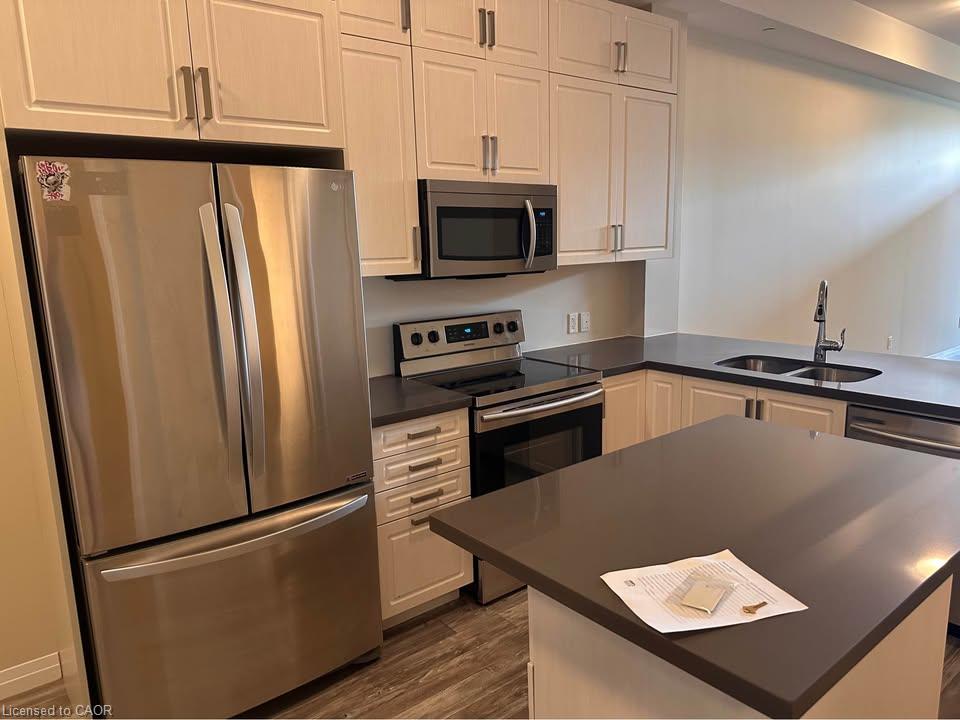 Kitchen featuring stainless steel appliances, light-toned cabinetry, dark countertops, a double basin sink, and wood-finish flooring