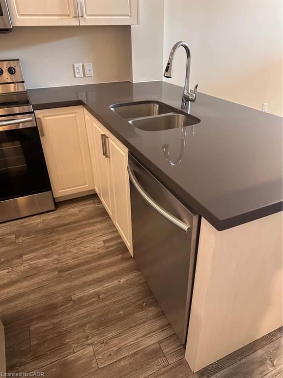 Kitchen featuring wood-finish flooring, white cabinetry, dark countertops, a double basin sink with a chrome faucet, and stainless steel appliances including a dishwasher and range