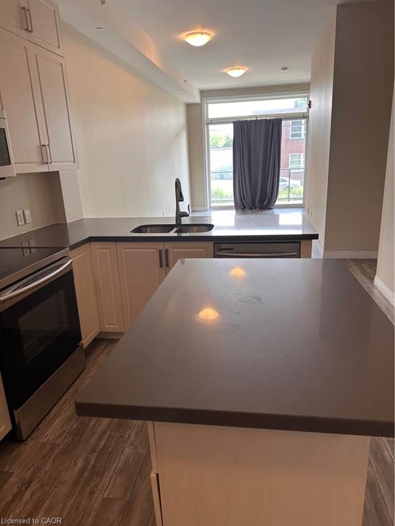 Kitchen featuring white cabinetry, dark countertops, wood-finish flooring, stainless steel appliances, and a built-in sink with a black faucet