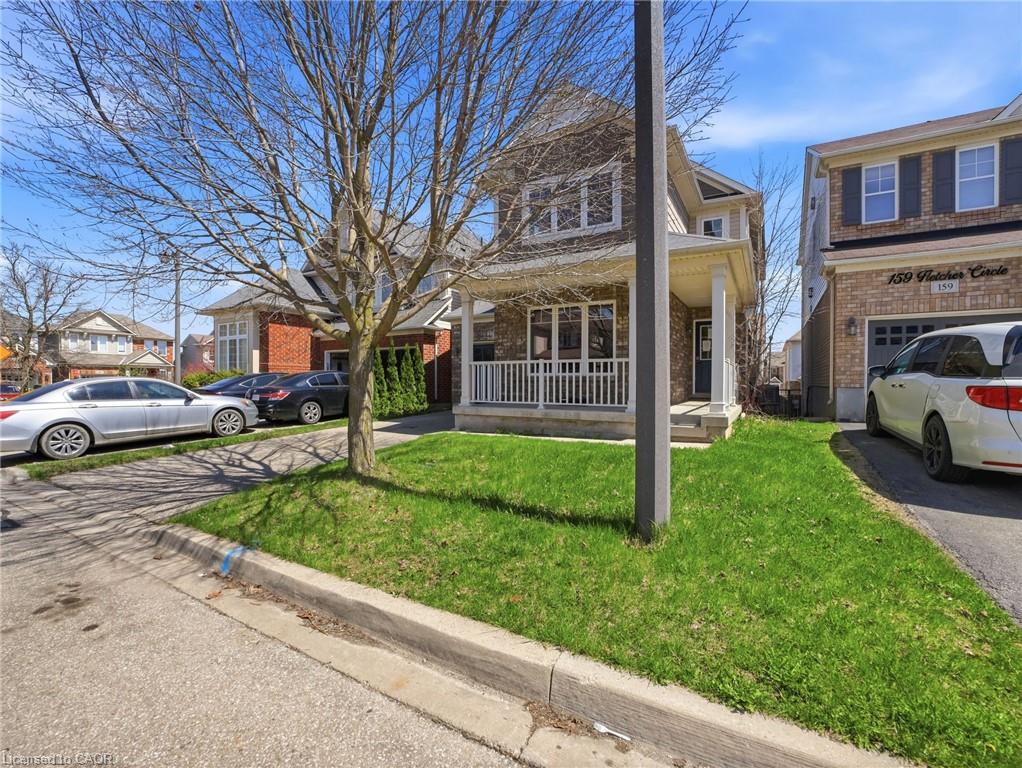 Two-story brick and siding residence featuring a covered front porch with white railing, a single-car driveway, and a front lawn with a mature tree