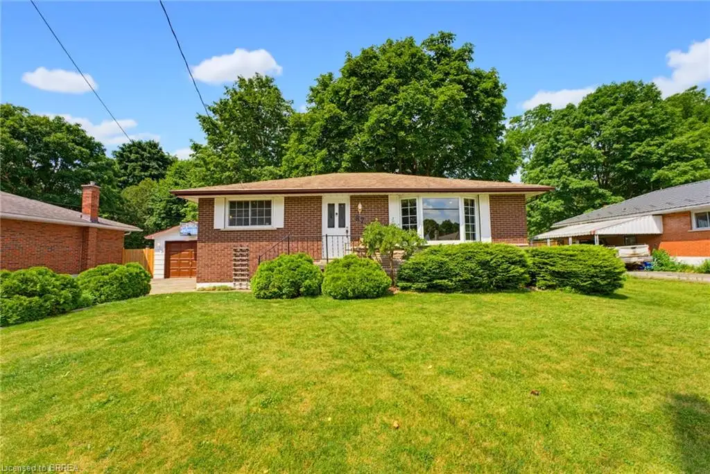 Brick exterior, attached garage with wood-finish door, front lawn with mature landscaping, and an expansive front window