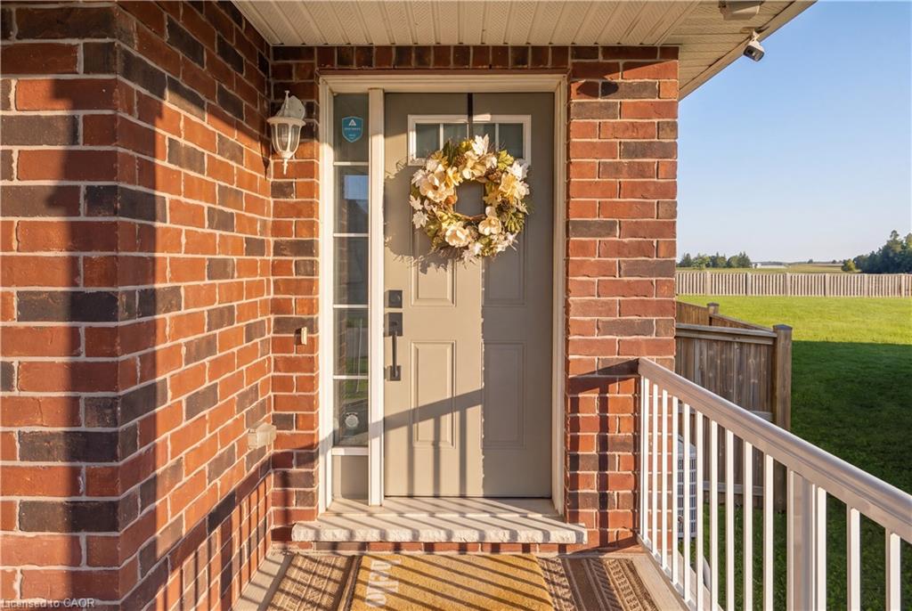 Brick exterior featuring a front entry door with a sidelite, a porch with white railings, and an outdoor wall sconce