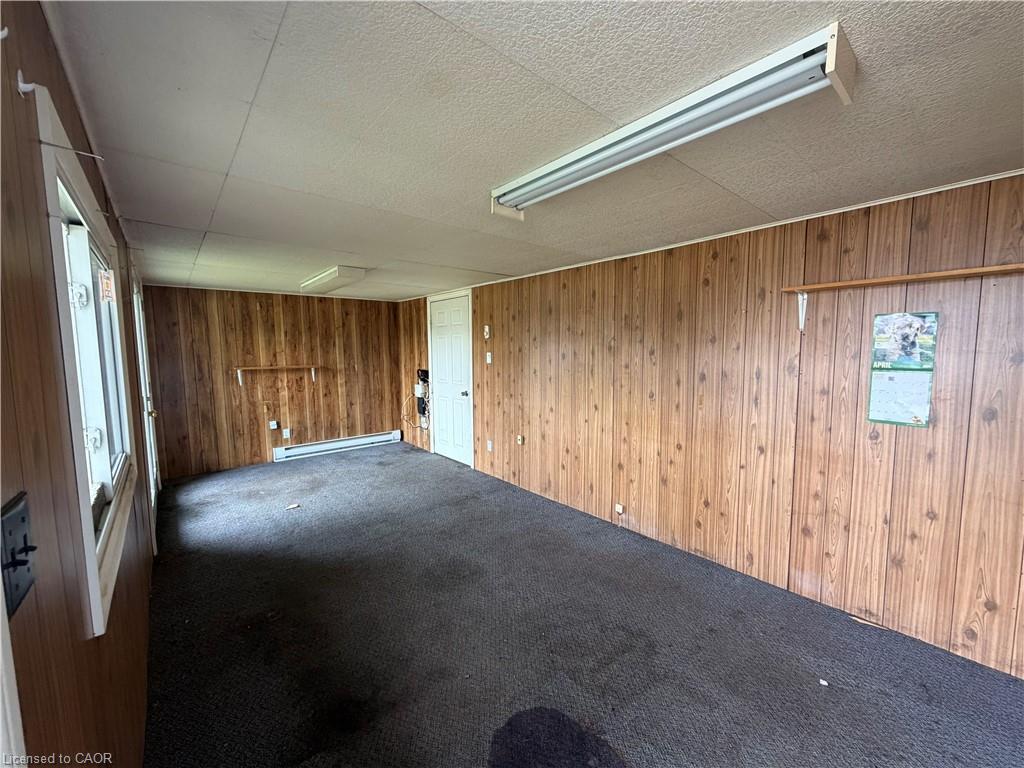 Wood-finish paneling, white door, wall-mounted heating unit, ceiling-mounted fluorescent lighting, and window with white trim