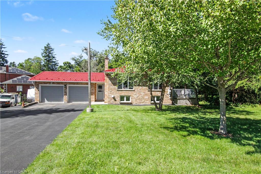 Brick exterior with a red metal roof, attached two-car garage, paved driveway, and mature landscaping