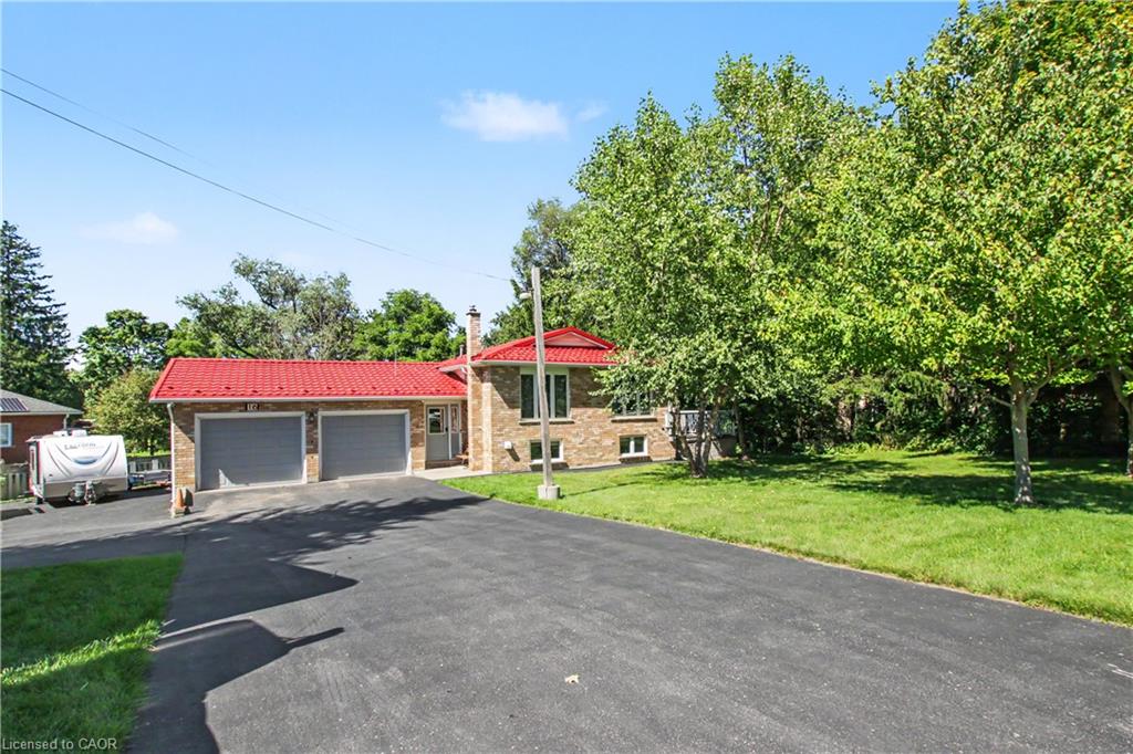 Brick exterior with a red metal roof, attached two-car garage, paved driveway, and mature trees